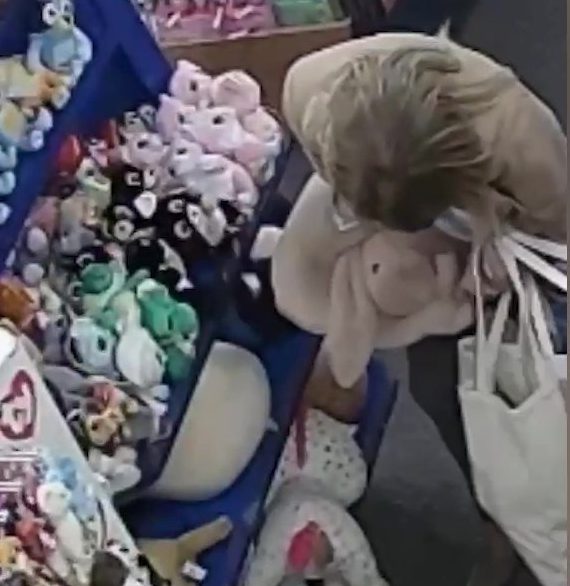 A video grab from CCTV footage showing a woman stealing a large Jellycat soft toy by stuffing it down her trousers.