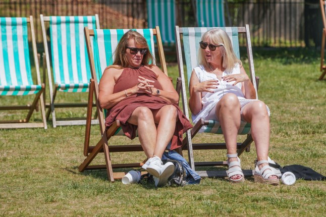 Two people relaxing on deck chairs in the warm sunshine in Green Park, London.